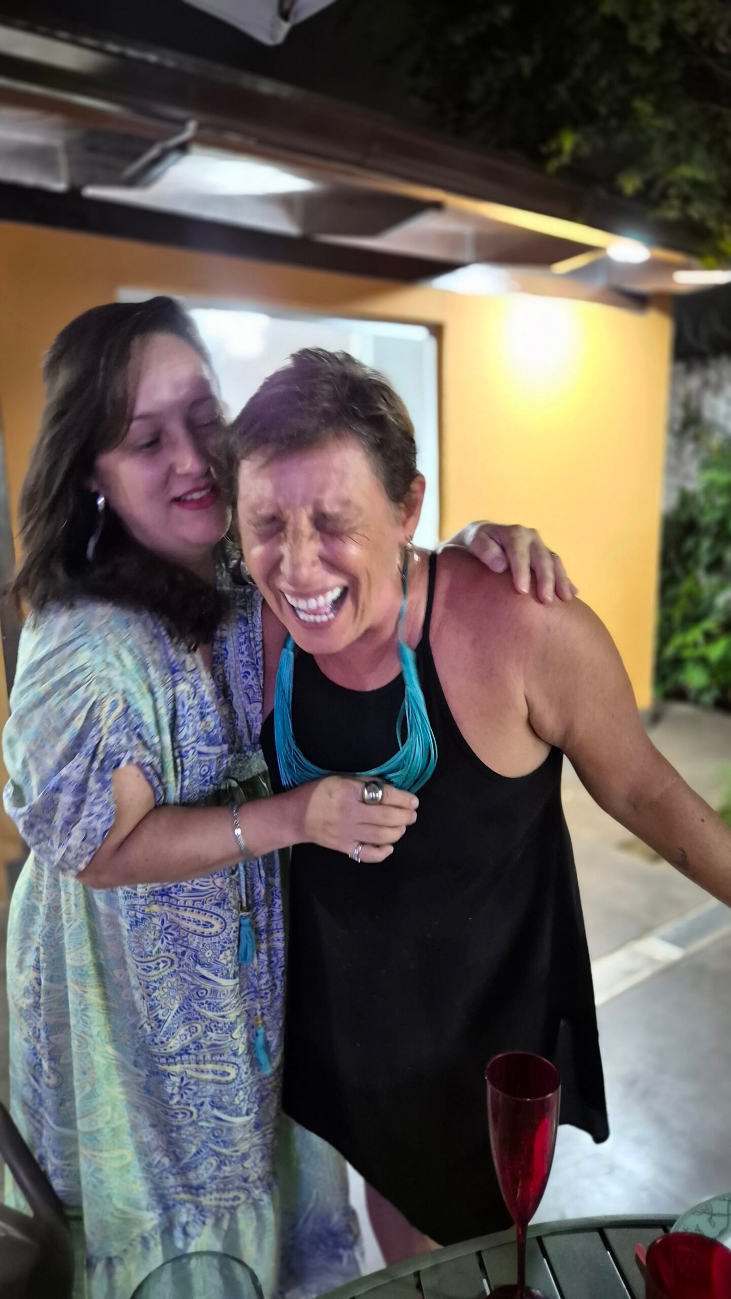 Duas mulheres rindo abraçadas, à noite