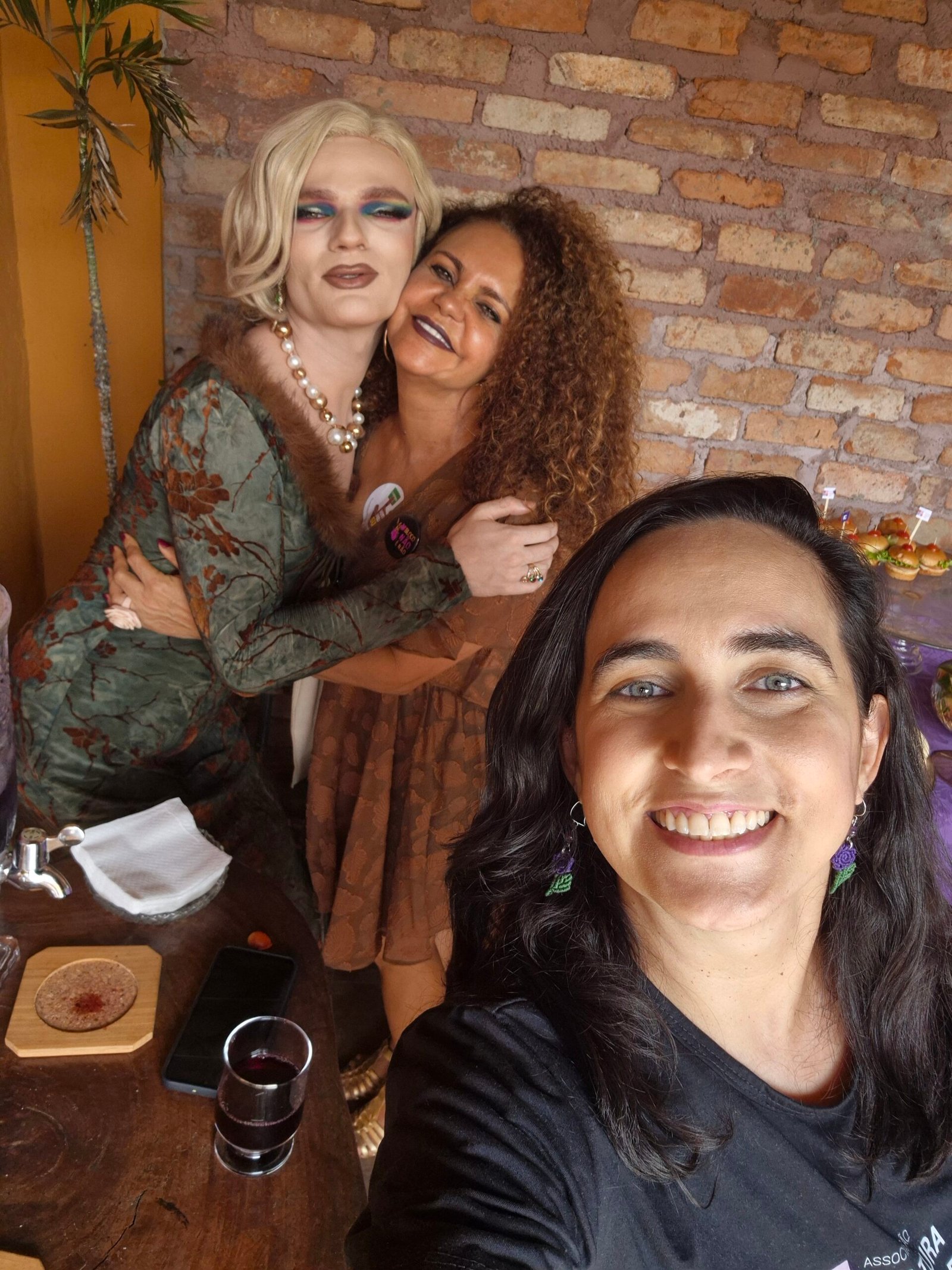 Três pessoas em uma selfie diante de uma parede de tijolos