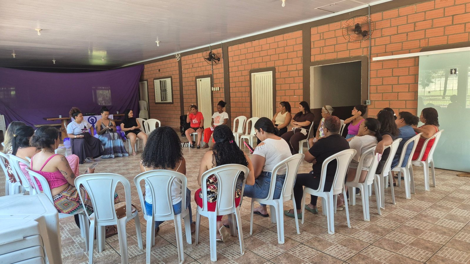 Roda com dezenas de mulheres no Emancipa, num salão de tijolos